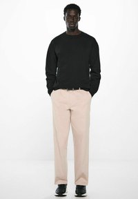 Schwarz sweatshirt mit langen Ärmeln, beige Hose und schwarze Sneakers. Gerader Schnitt, minimales Design, glatte Textur und neutrale Farben.