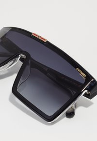 Occhiali da sole oversize neri con lenti grigie sfumate. Presentano dettagli in argento e una rifinitura rossa sul ponte. Made in Italy.