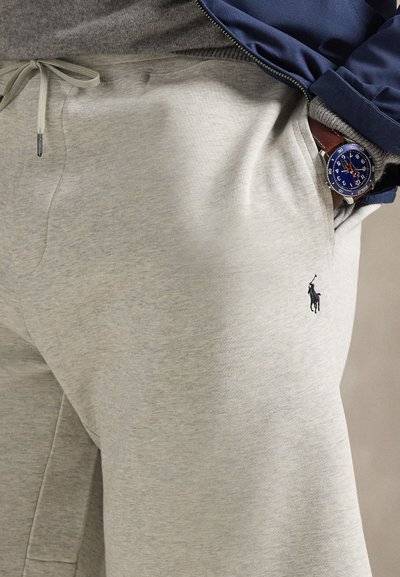 Light gray sweatpants made of soft fabric, featuring a drawstring waistband and a small black logo on the left leg. Smooth texture.