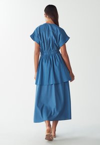 Modra obleka do kolen z kratkimi rokavi, zategnjeno pasu in plastenjem. Gladko blago, minimalističen slog, primeren za vsakodnevno nošenje.