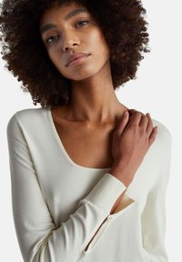 Krémový top s dlouhým rukávem, širokým kulatým výstřihem, žebrovanými manžetami a knoflíkovým detailem na boku. Měkká textura a přiléhavý střih.