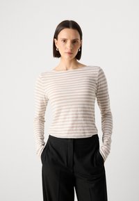 Langermet topp i lys beige med horisontale striper, laget av myk stoff. Rund hals, figursydd design, kombinert med svarte bukser.