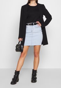 Černý dlouhý blazer, černý top, světlé modré džíny s třepeným lemem, černý opasek se stříbrnými kroužky, malá černá kabelka a robustní černé boty.