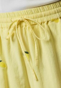 Pantalon jaune à taille élastique avec un cordon noué et de petits motifs de citron brodés sur un tissu doux.