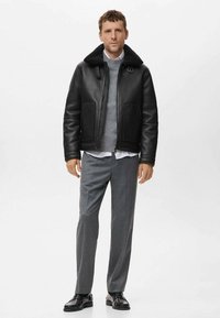 Chaqueta de cuero negro con un cuello de piel sintética, suéter de punto gris y pantalones grises. El conjunto presenta un diseño moderno y estructurado.