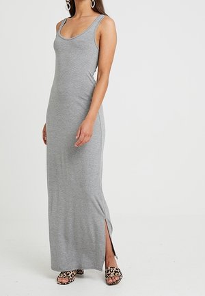 Kobieta ubrana w szarą, dopasowaną, bezrękawnikową suknię maxi z bocznym rozcięciem oraz sandały na otwartym palcu w panterkę na jednolitym tle.