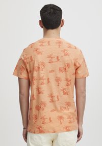 Kortermet, oransje T-skjorte med et tonalt palmetre-m�ønster. Laget av myk stoff med løs passform og rund hals.