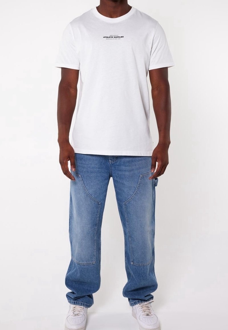 Vit bomull t-shirt med svart text, ihop med ljusblå, lösa denim cargobyxor med sidfickor och vita sneakers.