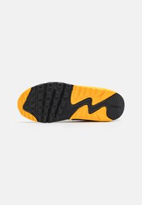Fekete és sárga sneaker talp, texturált gumival, kiemelkedő barázdákkal és hullámos mintázattal. Nike logó látható az oldalon.