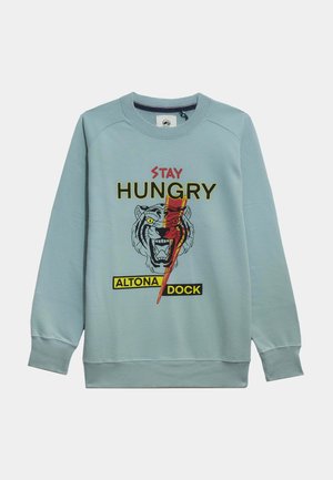 Sudadera azul claro con un gráfico de tigre, texto "STAY HUNGRY" y etiqueta "ALTONA DOCK" en amarillo. Textura suave con puños acanalados.