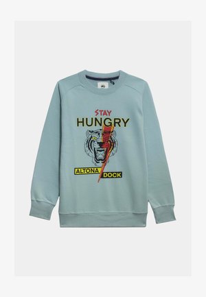 Sudadera azul claro con un gráfico de tigre, texto "STAY HUNGRY" y etiqueta "ALTONA DOCK" en amarillo. Textura suave con puños acanalados.