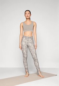 Beige crop top, amelyet illeszkedő, kígyóbőr mintás leggingsszel párosítanak, oldalsó hasítékokkal a bokáknál. Az öltözet sima, rugalmas anyagból készült.