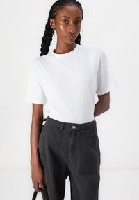 T-shirt en coton blanc à manches courtes, col rond, porté avec un pantalon taille haute gris foncé avec un bouton à l'avant.