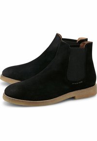 Bottines Chelsea en suède noir avec panneaux latéraux élastiques, accents tan et semelle en caoutchouc beige. Forme élégante avec un design à bout rond.