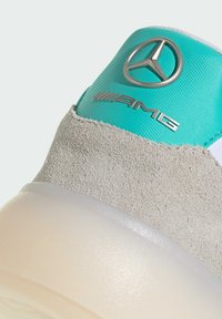Athletic shoe featuring a gray suede upper, turquoise accents, and a transparent sole. The shoe displays a metallic Mercedes-Benz logo.