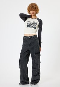 Crop top z czarnymi długimi rękawami i graficznym nadrukiem, w zestawie z luźnymi czarnymi spodniami cargo z wieloma kieszeniami i swobodnym krojem.