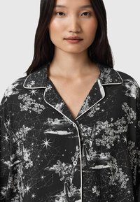 Czarna koszula piżamowa z kwiatowymi i kosmicznymi wzorami, z białymi lamówkami i luźnym krojem. Zapięcie na guziki, z kołnierzykiem.