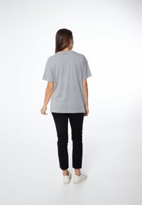 Camiseta gris de algodón con mangas cortas, corte relajado y cuello redondo, combinada con pantalones negros ajustados y zapatillas blancas.
