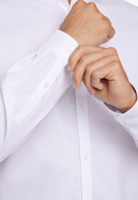 Witte langslibbige shirt met knoopmanchetten, gemaakt van gladde stof, met een klassieke kraag en heldere plastic knopen.