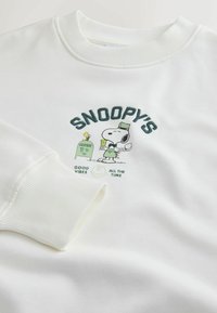 Bílá mikina s žebrovanými manžetami a grafikou Snoopyho, světle zeleným textem "SNOOPY'S GOOD VIBES ALL THE TIME." Měkká tkanina.