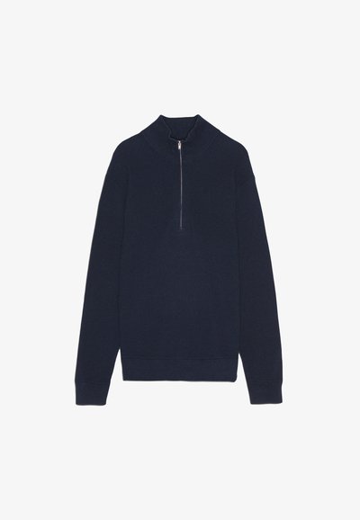 Marinblå stickad tröja med hög krage och silverfärgad dragkedja. Har ribbad struktur och långa ärmar. Enkel, avslappnad design.