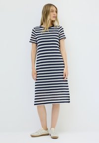 Knielanges gestreiftes Kleid aus marineblauem und weißem Strickstoff, runder Ausschnitt, kurze Ärmel, Seitenschlitze, kombiniert mit weißen Sneakers.