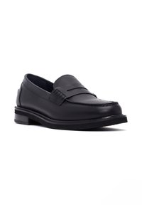 Mocasines de cuero negro con punta redondeada, costuras decorativas y una suela de goma baja. Textura suave y detalles de diseño minimalista.