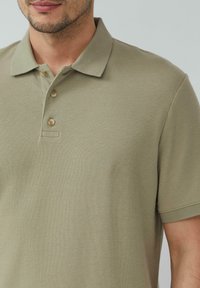 Khaki polo shirt met een gestructureerde stof, drie knoopsluitingen en korte mouwen. Heeft een klassieke kraag en een subtiel geweven patroon.
