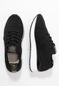 Black athletic shoes with a breathable mesh upper, soft lining, and a white cushioned sole. Features a logo on the tongue and heel tab.