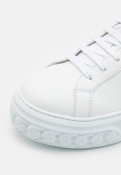 Baskets en cuir blanc avec semelle en caoutchouc texturé, bout rond et lacets plats blancs. Présente des coutures contrastées et un design minimaliste.