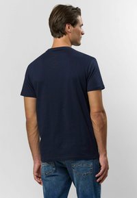 Námořnická modrá bavlněná tričko s krátkým rukávem a kulatým výstřihem, zobrazené ze zadní strany. Má hladké, ležérní střih.