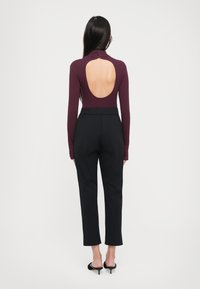Bodysuit dengan kerah tinggi dan punggung terbuka berwarna burgundy tua, dipadukan dengan celana hitam berkualitas tinggi dengan pinggang tinggi, memiliki potongan yang disesuaikan dan panjang cropped.