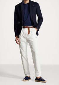 Marinblå kavaj över en marinblå t-shirt, vita byxor, brunt flätat bälte. Blå espadriller med broderade detaljer fulländar outfiten.