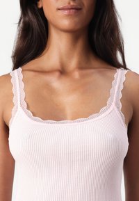 Top tank rosa chiaro a coste con spalline in pizzo ondulato e scollatura. Texture morbida, design aderente, adatto per essere indossato a strati o per un look casual.