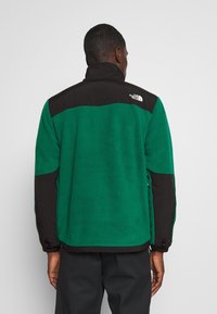 Fleece bunda s zeleným tělem, černými rameny a límcem. Logo na zadní straně; textured povrch se zapínáním na zip a nastavitelné manžety.