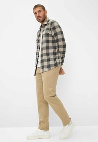 Karierte Flanellshirt in Grau und Beige, mit Knopfleiste, kombiniert mit beigen Chinos und weißen Sneakern, im lässigen Schnitt.