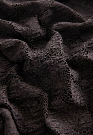 Tissu noir avec des motifs en dentelle complexes, présentant une surface texturée et un drapé doux, mettant en valeur des coutures détaillées et des découpes.