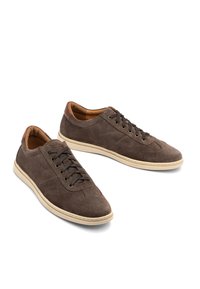 Zapatillas de ante marrón con un perfil bajo, puntera redonda y cierre de cordones. Acentos de cuero en el talón y suela de goma color crema.