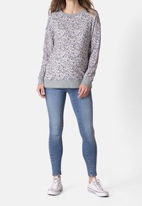 Pull en léger gris avec un motif moucheté de nuances bleues et violettes, col et poignets côtelés, associé à un jean slim bleu et des baskets blanches.