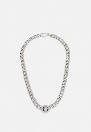 Zilveren ketting met dikke schakels en een ronde zwarte hanger met een getextureerd leeuwenkopontwerp in het midden.