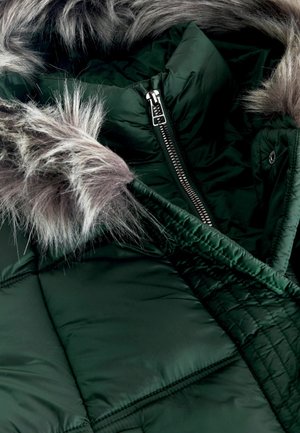Geacă puffer de culoare verde închis, cu fermoar frontal, având un detaliu de glugă din blană sintetică gri detașabil și o textură matlasată.