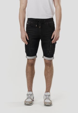 Fekete farmer rövidnadrág felhajtott szegéllyel, két nagy oldalzsebbel, húzózsinóros derékpánttal és kontrasztos varrási részletekkel.