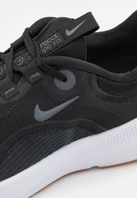 Zapatilla de running negra de Nike con parte superior de malla, suela de goma, acentos texturizados y marca en gris. Presenta un collar acolchado y un sistema de cordones.