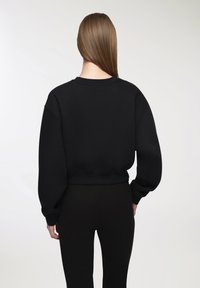Felpa nera corta con maniche lunghe e gonfie e collo rotondo, realizzata in tessuto morbido e testurizzato. Indossata con pantaloni neri abbinati.