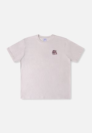 T-shirt rose clair à manches courtes avec un petit tigre de dessin animé ludique tenant une fleur imprimé sur le côté gauche de la poitrine.