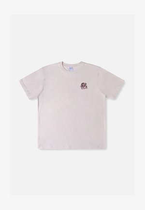T-shirt rose clair à manches courtes avec un petit tigre de dessin animé ludique tenant une fleur imprimé sur le côté gauche de la poitrine.