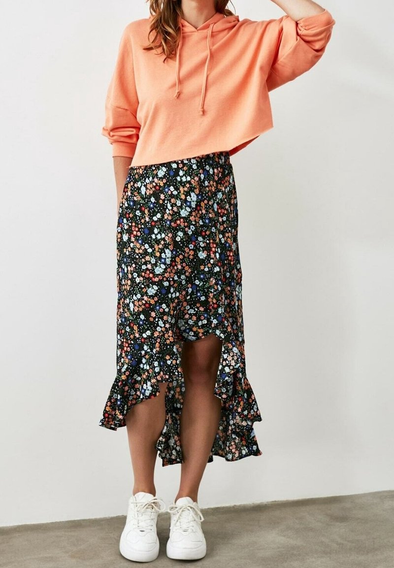 Sudadera recortada color coral, falda negra floral con dobladillo con volantes, decorada con flores multicolores, combinada con zapatillas blancas.