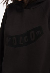 Mustapaita, jossa on hieman kohotettu teksti logo "VOLCOM" kontrastivärillä, rento leikkaus ja teksturoitu kangas.