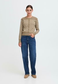 Beige stripete cardigan med rund hals, knappelukking og ribbestrikket kant, kombinert med blå rette jeans og brune slip-on sko.
