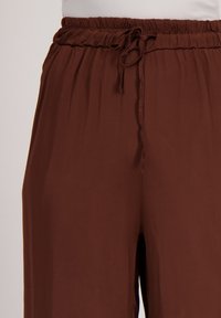 Lichte bruine broek met een elastische tailleband en trekkoord. Kenmerkt zich door een gladde textuur en een ontspannen pasvorm.